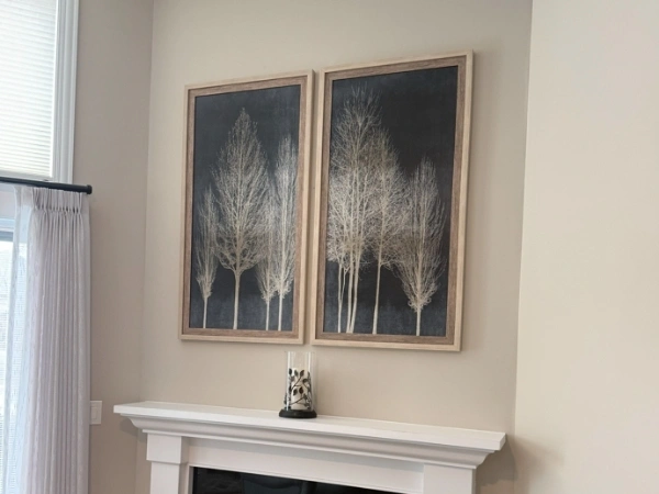 Two framed tree pictures mounted above a white fireplace mantel