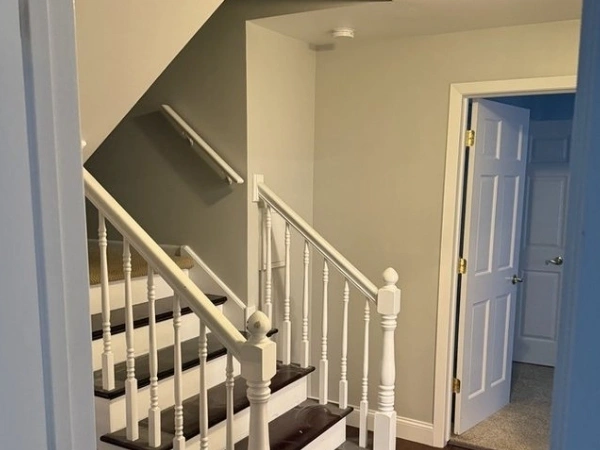 Interior staircase and hallway with white railings, dark stair treads, finished walls, trim, and adjoining doors
