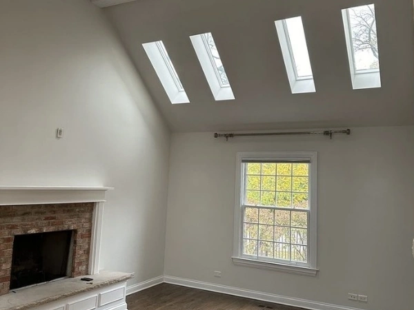 Tall living room with four skylights, ceiling beams, fireplace, white trim, and wood flooring
