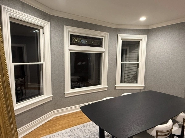 Finished dining room with gray wallpaper, white crown molding, detailed window trim, and wood flooring